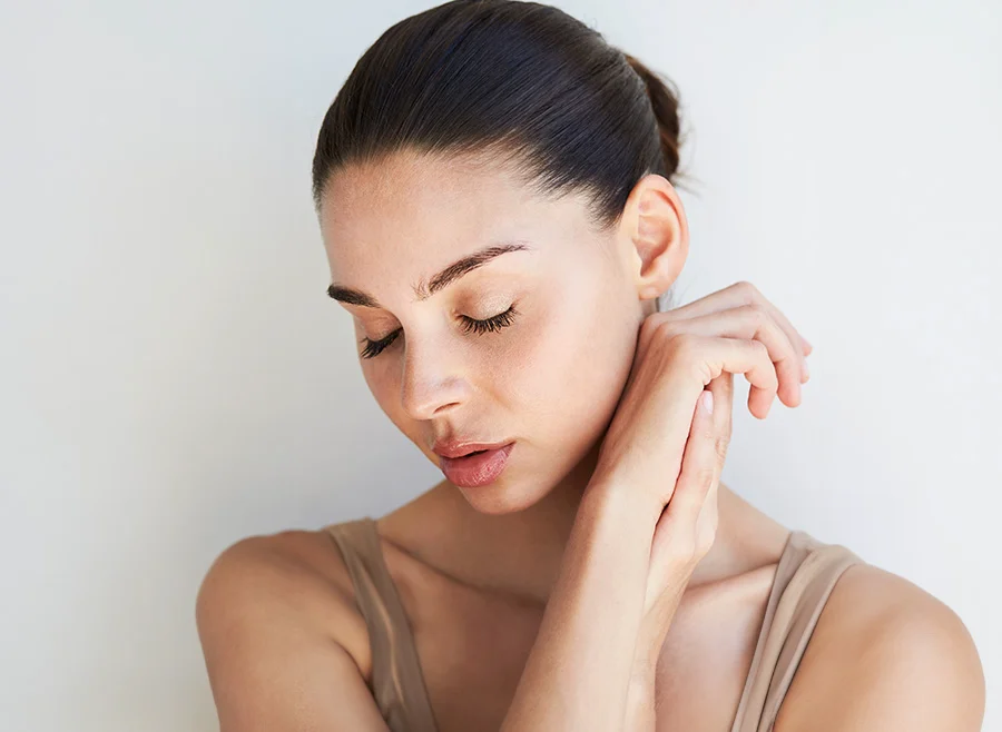 Woman with her hair pulled back, gently holding her arms with a calm expression, eyes closed, against a light background - Cheek Fillers in North Carolina