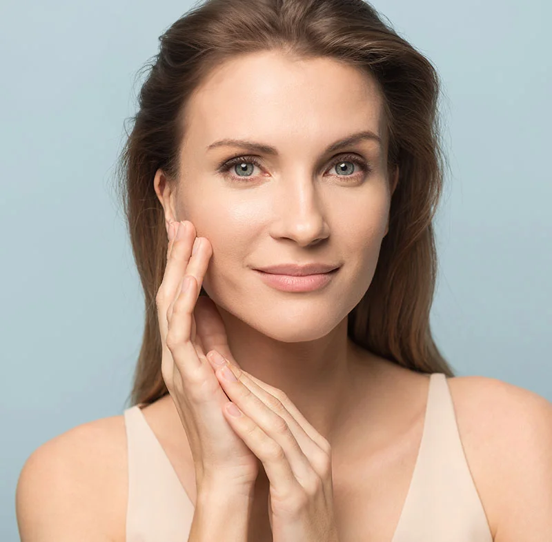 A woman with light brown hair gently touching her face, with a calm and serene expression against a soft blue background - IPL Photofacial BBL in North Carolina