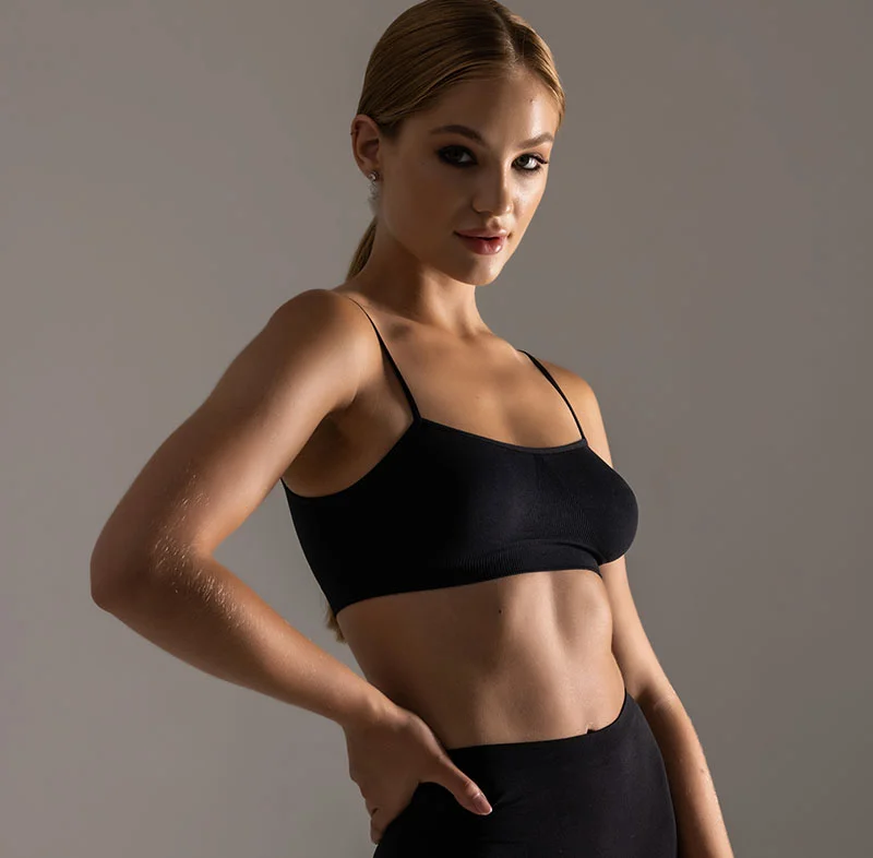 A woman with blonde hair, dressed in a black sports bra, stands confidently with a strong pose, looking directly at the camera - Laser Hair Removal in North Carolina